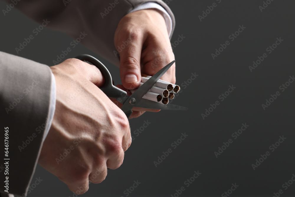 Stop smoking concept. Man cutting cigarettes on gray background, closeup with space for text