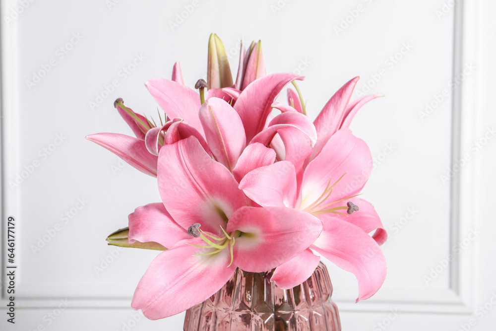 Beautiful pink lily flowers in vase against white wall, closeup Beautiful pink lily flowers in vase against white wall, closeup