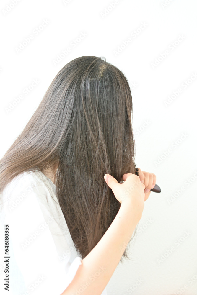 Fototapeta premium ブラシで髪をとかす若い黒髪の女性の後ろ姿