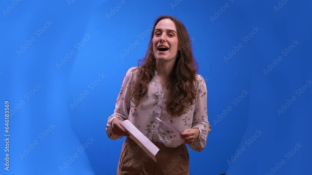 Woman announcer with curly hair opens envelope to announce winner of show. Announcer looking for winners with puzzled look on face at blue chromakey wall Woman announcer with curly hair opens envelope to announce winner of show. Announcer looking for winners with puzzled look on face at blue chromakey wall