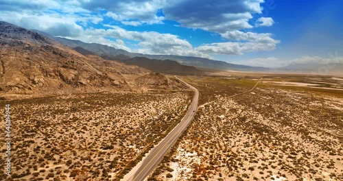 Lonely car moving by the empty highway in hot desert of Death Valley, California. Panorama of a dry desert and mountains from top view.