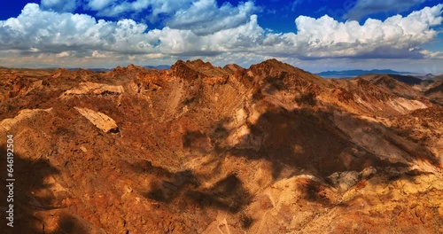 Approaching bare brown rocks in the Mojave desert. Rocky landscape under blue cloudy sky from aerial view. photo