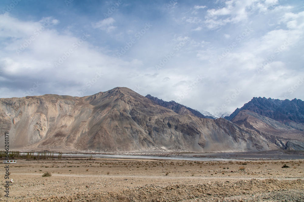 Fototapeta premium Scenic view of Himalayas and Ladakh ranges. Beautiful barren hills in Ladakh with dramatic clouds in the background. View from the road from Nubra Valley to Turuk. Siachen area in Leh Ladakh.