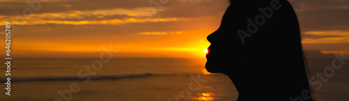 Silhouette of a girl backlit, kissing the sun in front of the sea at sunset. Space for text.