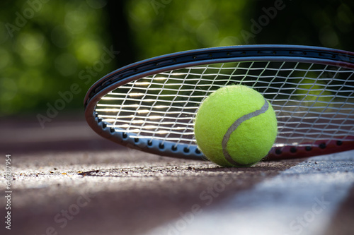 Tennis racquet and yellow tennis ball on outdoor court © NetPix