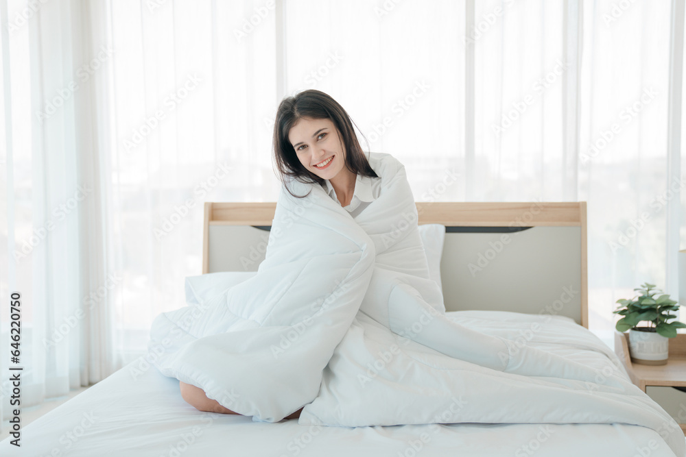 Photo of young happy woman in pajama stretching her arms and smiling while sitting on bed after sleep Photo of young happy woman in pajama stretching her arms and smiling while sitting on bed after sleep