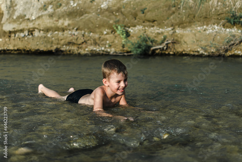 a preschool-age boy in bathing trunks plays sitting in the river