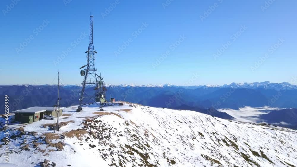 An aerial pass over a snow-covered New Zealand mountain, highlighting a sturdy communications tower amid pristine winter scenery. Perfect for conveying the blend of nature and technology An aerial pass over a snow-covered New Zealand mountain, highlighting a sturdy communications tower amid pristine winter scenery. Perfect for conveying the blend of nature and technology
