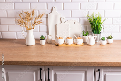 White ceramic utensils and kitchen utensils on a wooden countertop in an eco-friendly kitchen with green indoor plants. Cozy house.