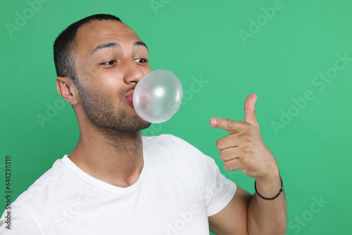 Man blowing bubble gum on green background. Space for text