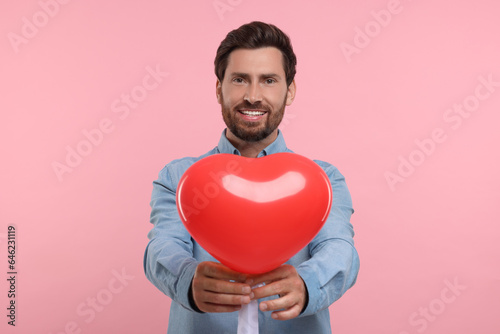 Happy man holding red heart shaped balloon on pink background © New Africa