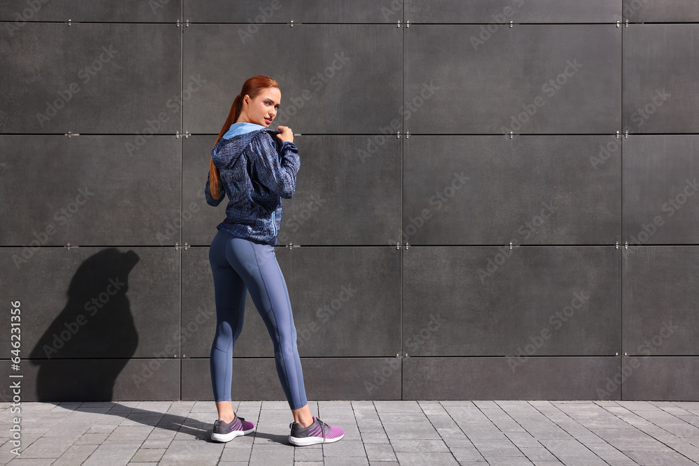 Beautiful woman in stylish gym clothes near dark grey wall on street, space for text Beautiful woman in stylish gym clothes near dark grey wall on street, space for text