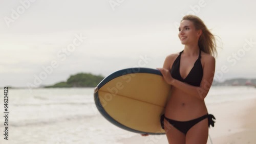 4K Portrait of Young woman surfer in bikini holding surfboard walking on the beach 