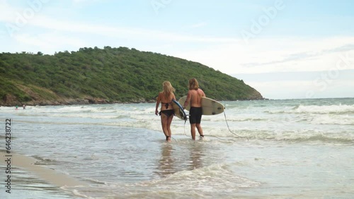4K Group of friends in swimwear holding surfboard and walking together on the beach at summer sunset.