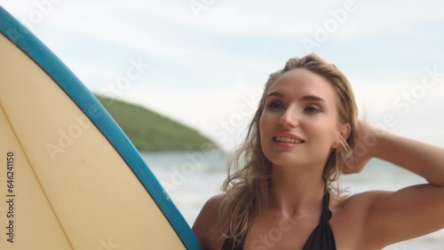 Portrait of happy woman holding surfboard standing on sunny beach 