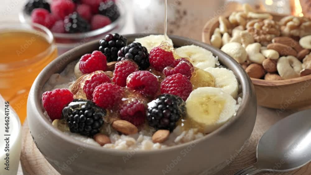 Honey is poured into a breakfast bowl. Oatmeal with fresh berries, nuts, and banana fruit. Healthy food concept.