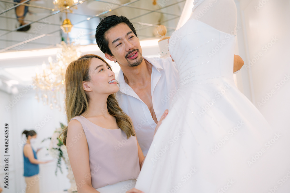 Attractive Bride and groom is smiling while choosing wedding dress in modern wedding salon.