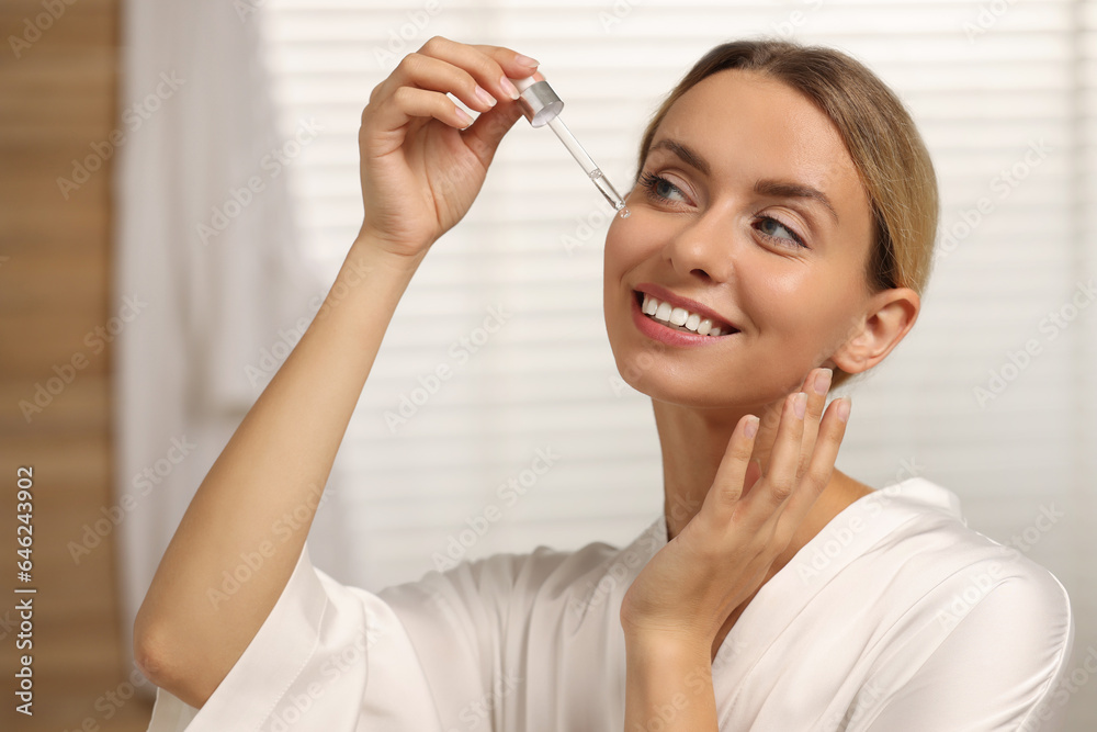 Beautiful woman applying cosmetic serum onto her face in bathroom Beautiful woman applying cosmetic serum onto her face in bathroom