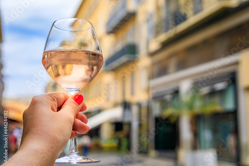Fototapeta Naklejka Na Ścianę i Meble -  Woman s hand holding a glass of rose provencal wine at an outdoor restaurant with a background of blurred buildings in Old Town Nice, South of France