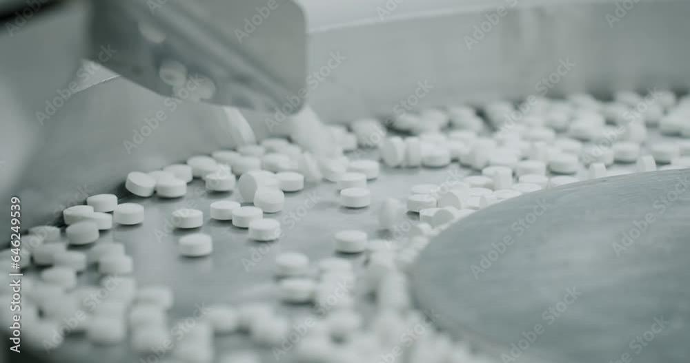 White pills moving on metal automatic line in workshop of pharmaceutical factory. Factory equipment and machine conveyor. Industrial pharmaceutical concept. view of drugs move along conveyor belt.