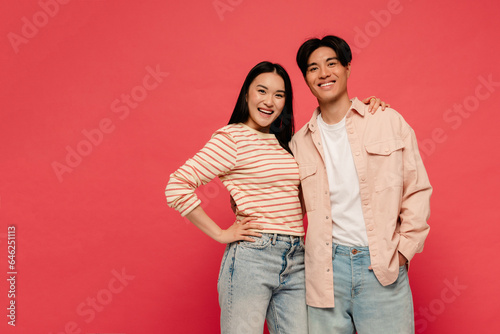 Asian man and woman smiling while standing isolated over red background