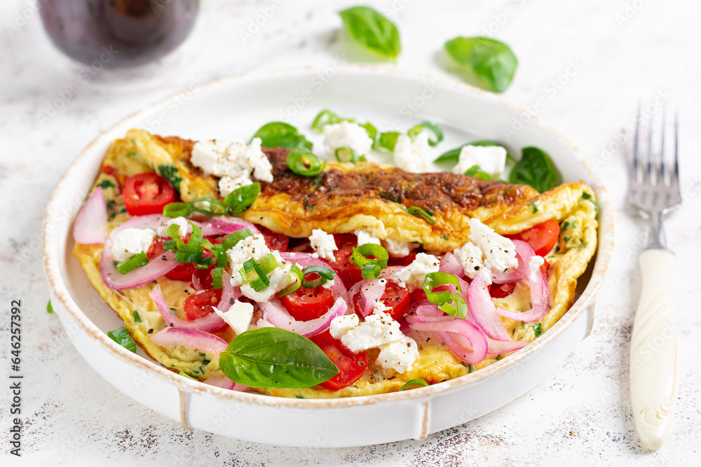 Omelette with tomatoes, feta cheese and red onion on white plate.  Frittata - italian omelet.