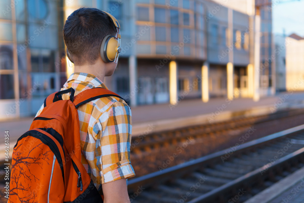 Fototapeta premium a student poses at a railway station, a teenage boy walks along the platform to the train, he has a backpack and books, goes to study, the concept of education