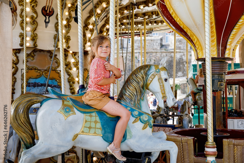 Happy positive preschool girl having a ride on the old vintage merry-go-round in city of St Malo France. Smiling child on a horse.
