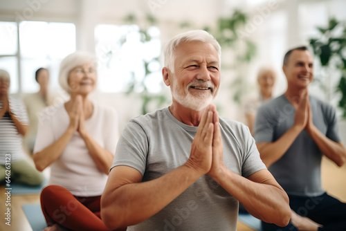 Group of active senior women doing a yoga class with friends and retirement home caregiver with a smile. Elderly group doing yoga exercise in a fitness center. Health and retirement self care