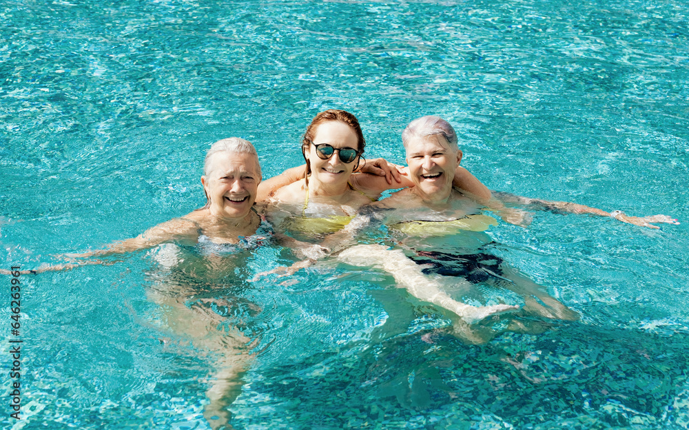 Three active mature senior caucasian friends women have fun in outdoor swimming pool under the sunlight. Vacation and healthy lifestyle concept