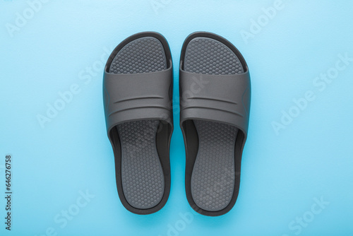 Dark gray black foam slippers on light blue table background. Pastel color. Closeup. Top down view. Male summer footwear.