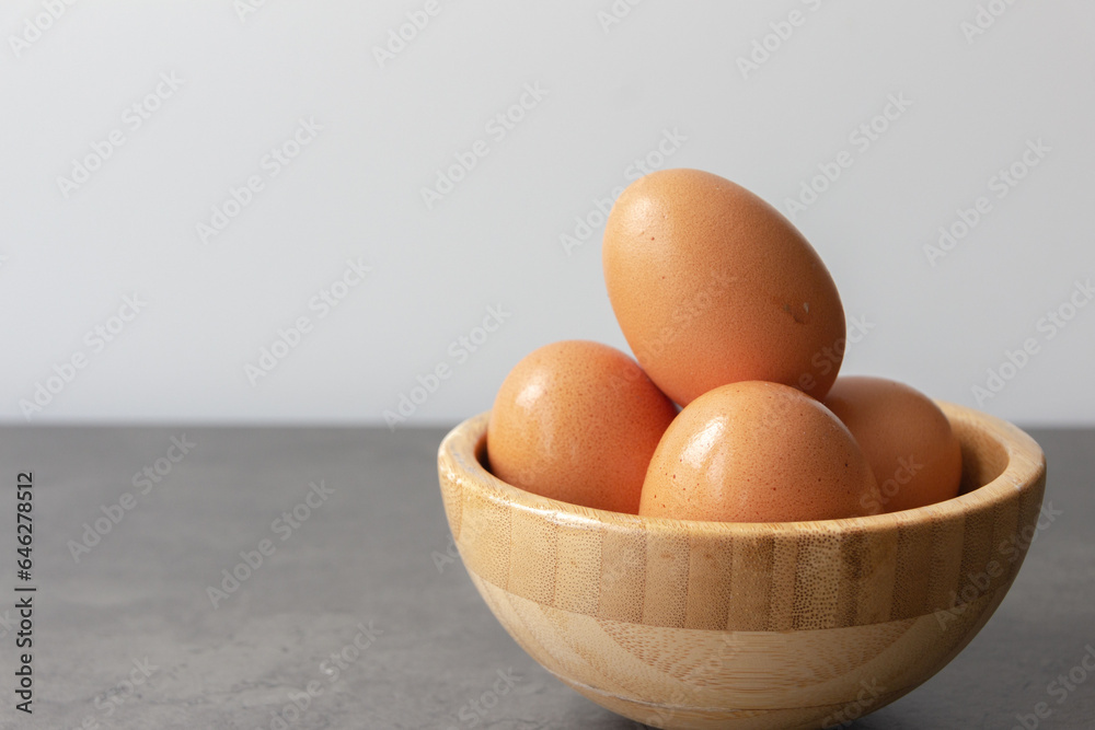 Four Fresh Eggs Stacked in Bamboo Bowl on Gray Table (With Copy Space) Four Fresh Eggs Stacked in Bamboo Bowl on Gray Table (With Copy Space)