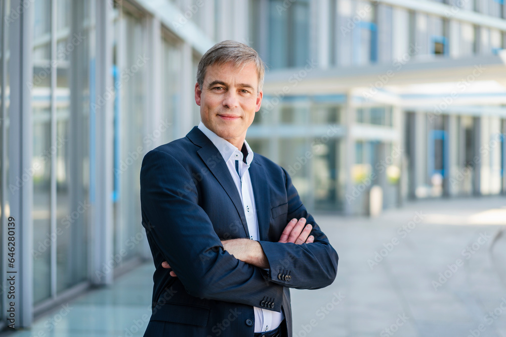 Confident businessman standing in office building with arms crossed Confident businessman standing in office building with arms crossed