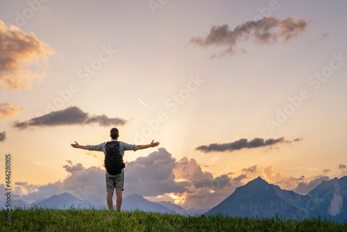 Hiker with arms outstretched looking at mountain range in meadow photo