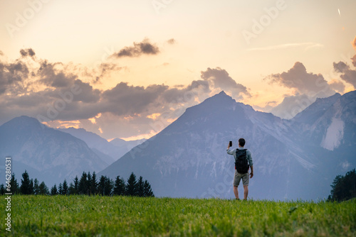 Hiker taking picture of mountains on smart phone in meadow photo