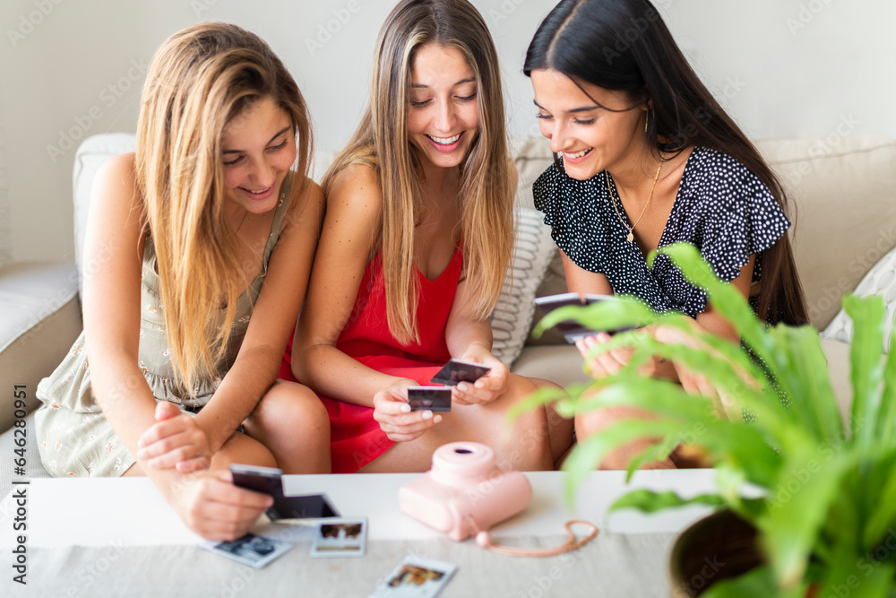 Happy friends looking at photographs sitting on sofa at home Happy friends looking at photographs sitting on sofa at home