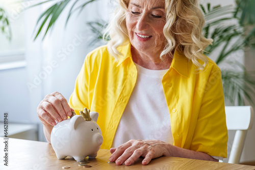 Happy senior woman saving money in piggy bank photo