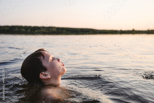 Boy spitting water in lake at sunset photo