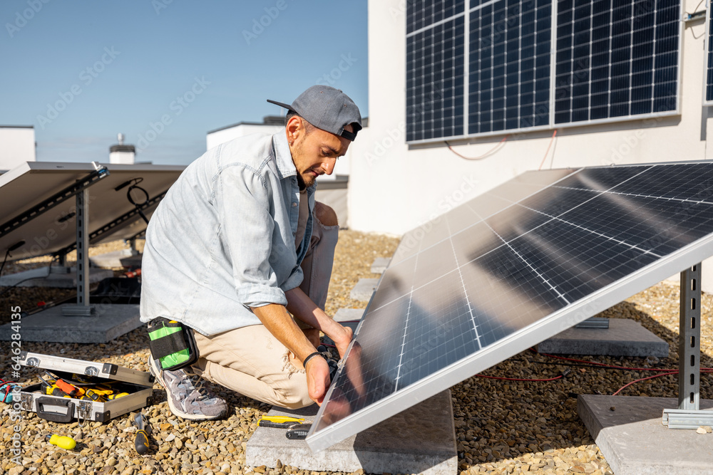 Man installing solar panels on the roof of his house, screwing cell on flat rooftop for self consumption. Renewable energy and sustainability concept Man installing solar panels on the roof of his house, screwing cell on flat rooftop for self consumption. Renewable energy and sustainability concept