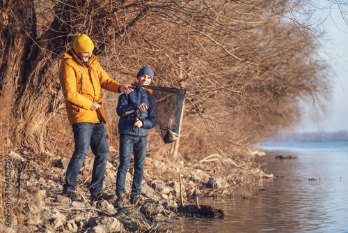 Father and son are fishing on sunny winter day. They caught a fish and are holding it in a landing net.