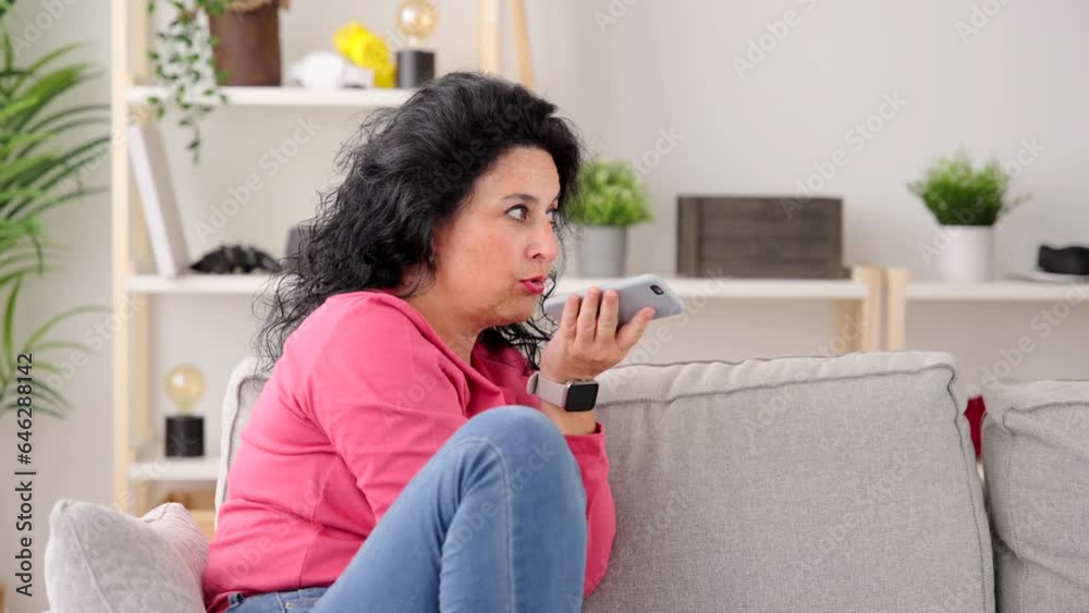Middle aged woman recording voice message on phone. Person sitting on sofa sending voicemail. Middle aged woman recording voice message on phone. Person sitting on sofa sending voicemail.
