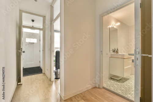 a bathroom with wood flooring and white walls in an apartment, taken from the front door to the hallway