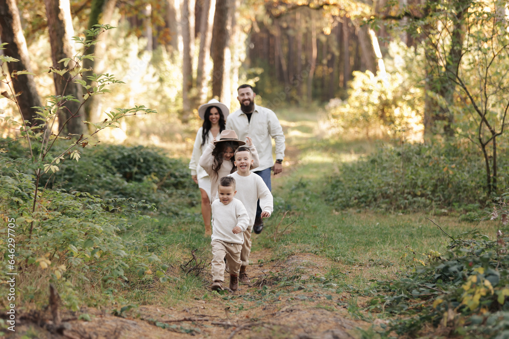 Young mother, father with daughter and sons are walking, having fun in autumn forest. Family holding hands enjoying time together at background of trees. Happy parenthood and childhood concept. Young mother, father with daughter and sons are walking, having fun in autumn forest. Family holding hands enjoying time together at background of trees. Happy parenthood and childhood concept.