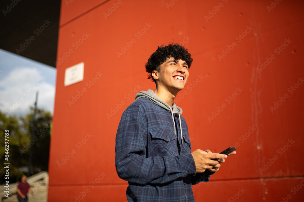 Fototapeta premium smiling young man with mobile phone by red wall