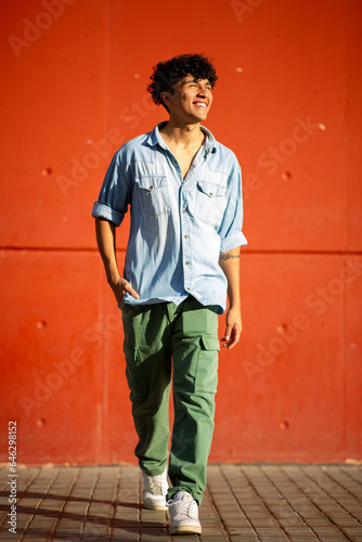 Full body happy young man walking by red wall