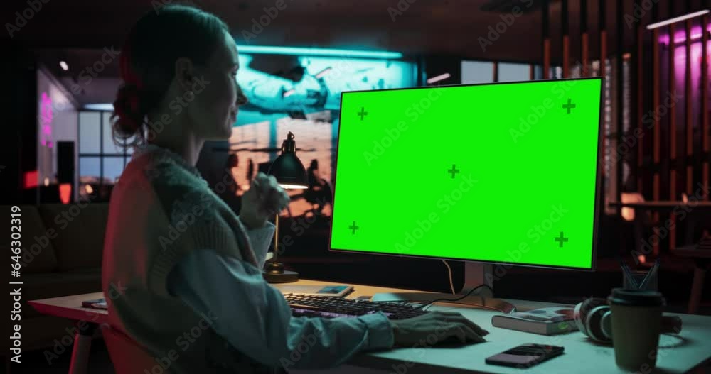 Over the Shoulder: Young Woman Sitting at Her Desk Using Desktop Computer with Mock-up Green Screen. Female Caucasian Specialist Working on Computer with Chroma Key Display at Creative Agency Over the Shoulder: Young Woman Sitting at Her Desk Using Desktop Computer with Mock-up Green Screen. Female Caucasian Specialist Working on Computer with Chroma Key Display at Creative Agency