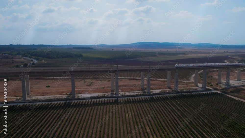 Train passes on a massive railway bridge over agricultural fields and vineyards - Colorful and cinematic shot with sun rays penetrating from the clouds (israel) - pull back reveal Train passes on a massive railway bridge over agricultural fields and vineyards - Colorful and cinematic shot with sun rays penetrating from the clouds (israel) - pull back reveal