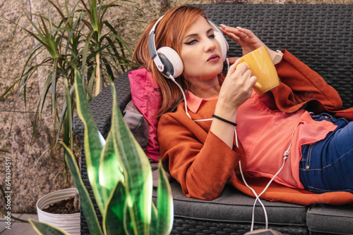 young woman relaxing on terrace sofa with headphones and cup of coffee photo