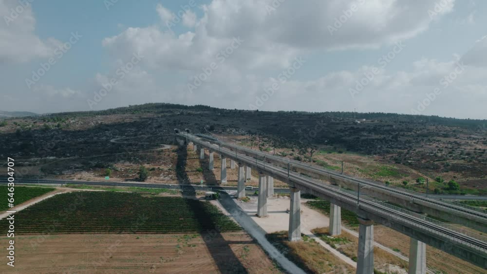 Train leaving a tunnel cut in the mountain and passing on a massive railway bridge over a road with cars and agricultural fields - Aerial parallax Train leaving a tunnel cut in the mountain and passing on a massive railway bridge over a road with cars and agricultural fields - Aerial parallax