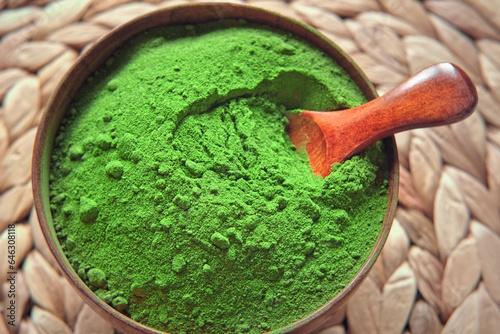 Wooden spoon with powdered matcha tea in a bowl spinning on natural background. Matcha powder. Top view, Closeup. Finely ground green powder. Japanese culture. Healthy eating with high antioxidants.